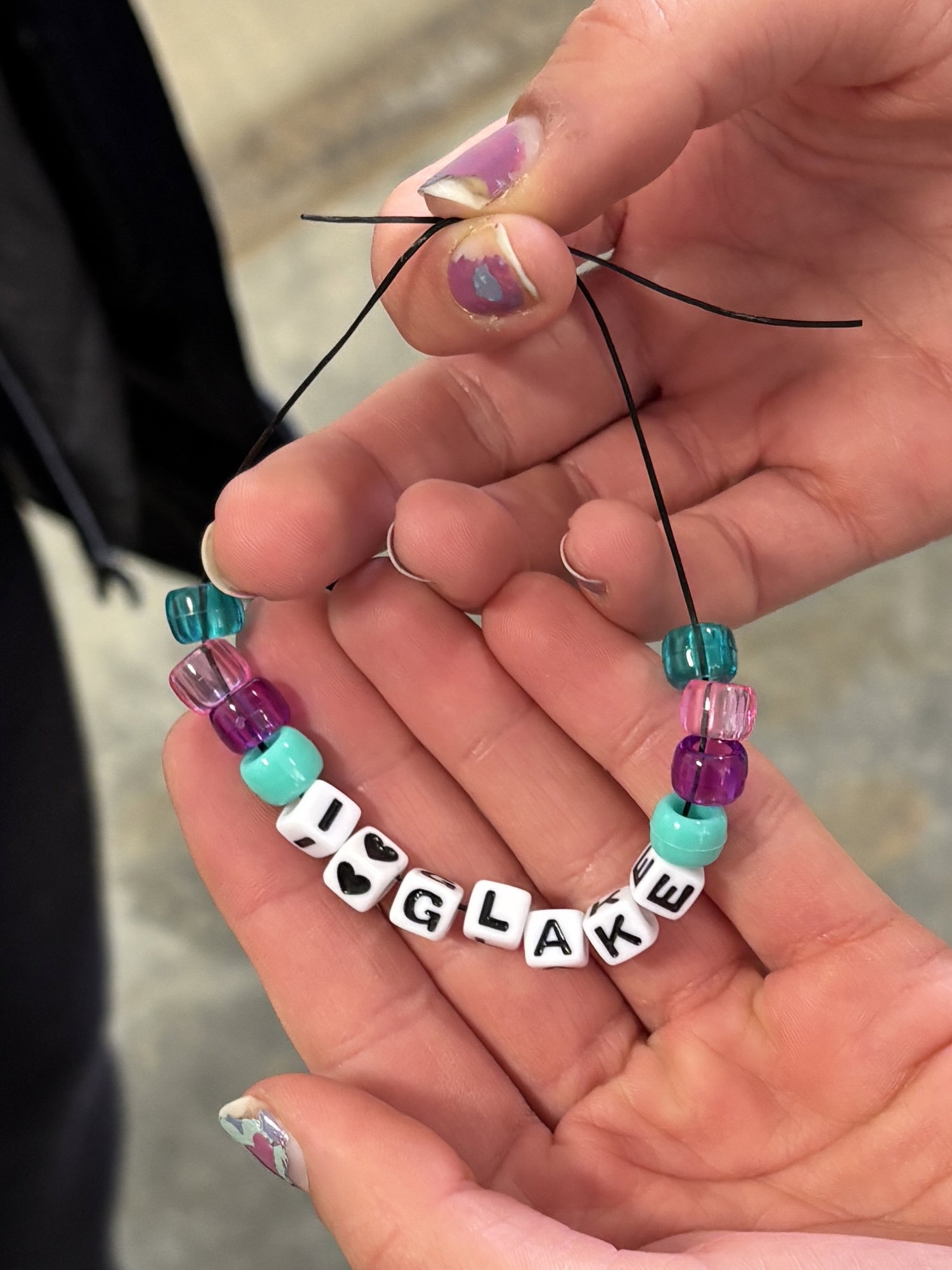 A beaded bracelet spelling "I love G Lake" held in a pair of hands